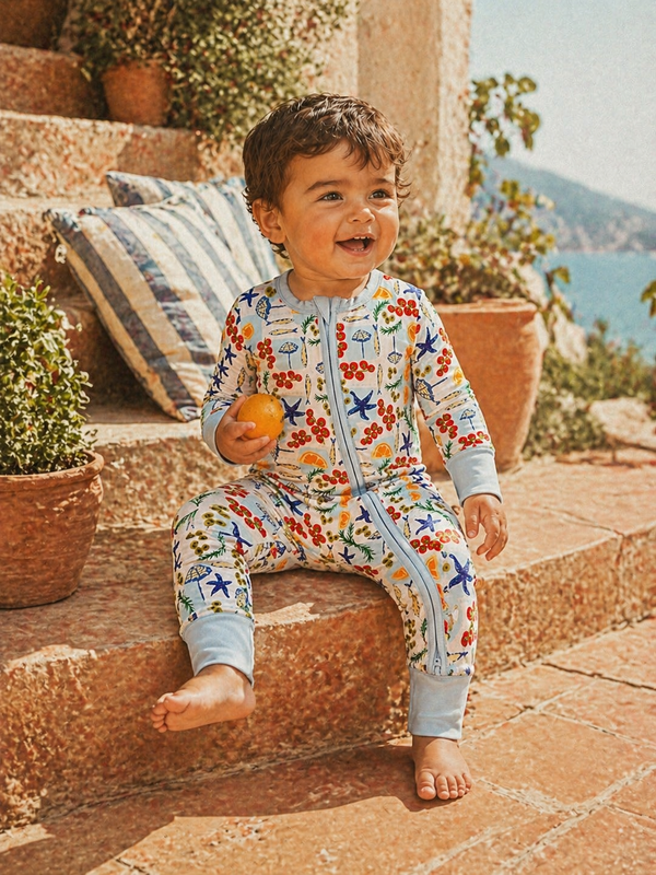 Smiling child in colorful play suit, sitting on stone steps with potted plants and a serene outdoor background.