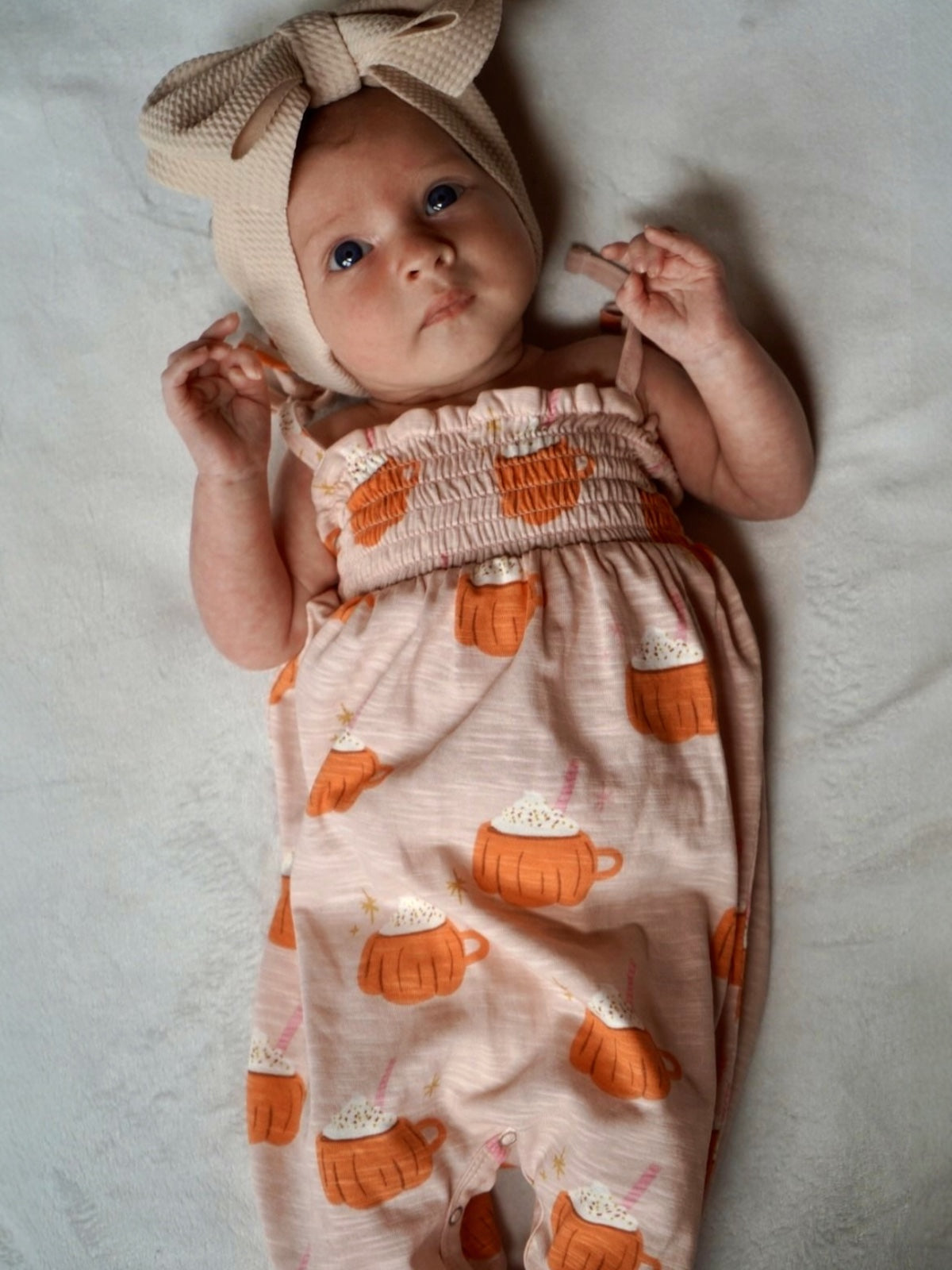 Baby in a cute outfit with a bow headband, featuring playful mug designs on a light pink background.