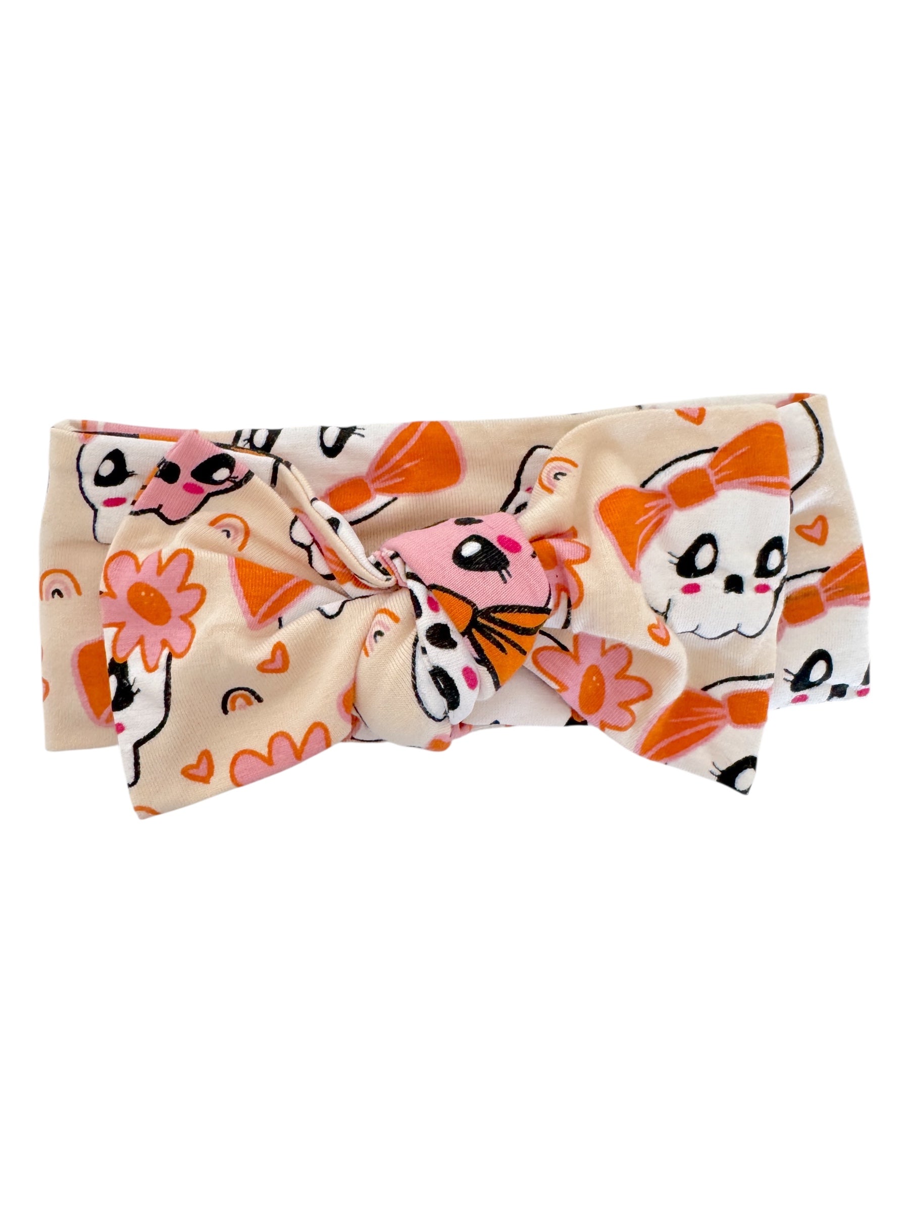 Colorful headband with a bow, featuring cute skulls and floral patterns on a beige background.