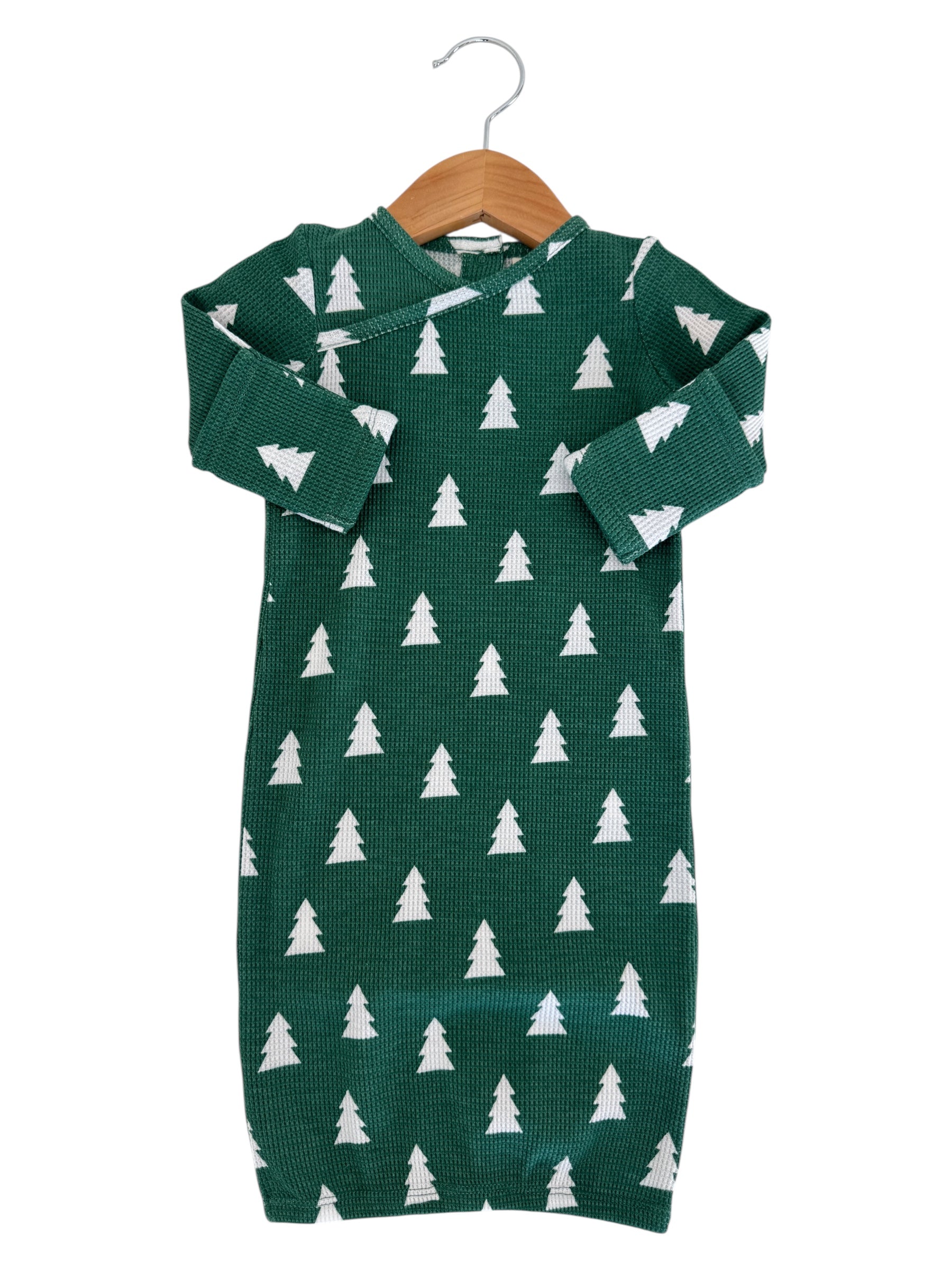 Green infant dress with white pine tree pattern, displayed on a wooden hanger.