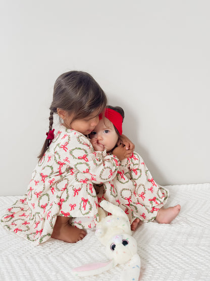 Two young girls in matching dresses embrace, with a plush bunny toy on a textured blanket. Bright, playful scene.