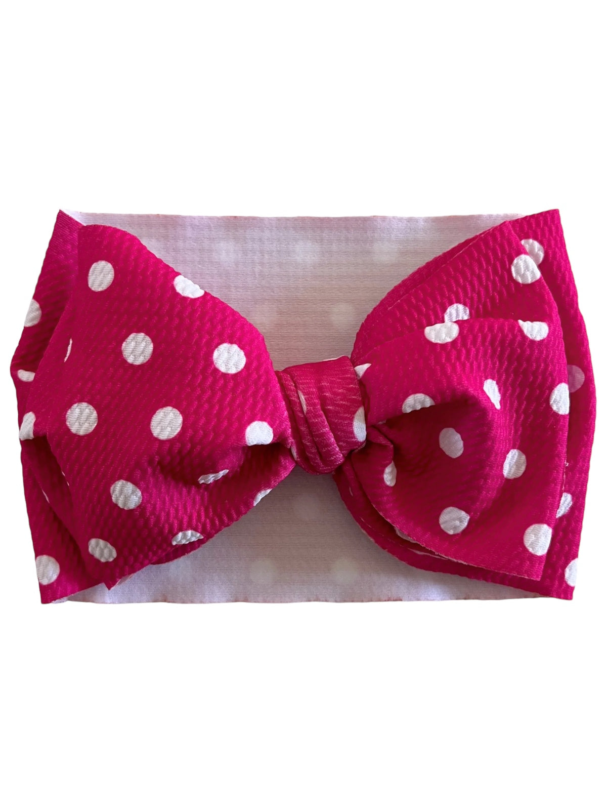 Bright pink headband with large white polka dot bow, set against a soft white background.