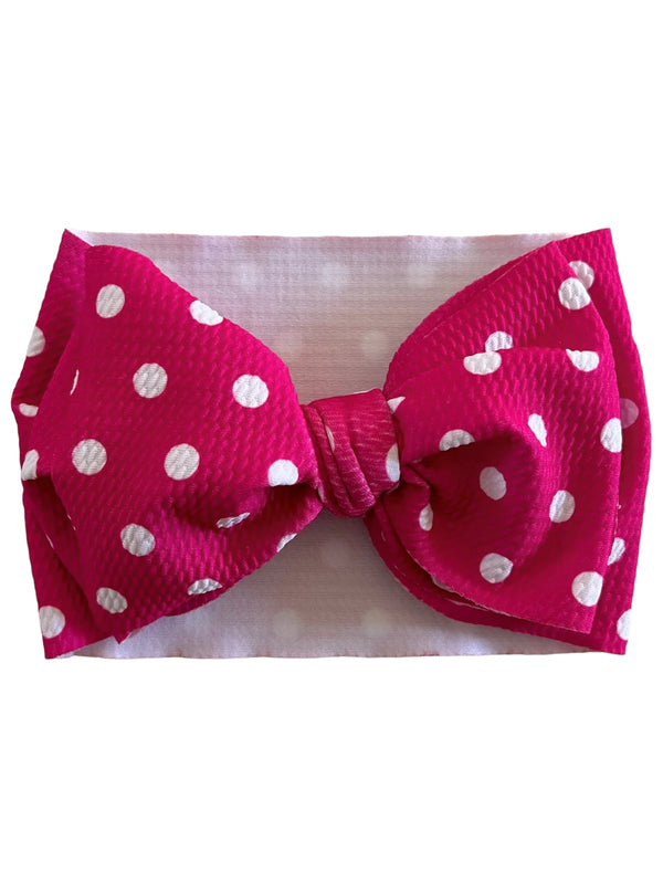 Bright pink headband with large white polka dot bow, set against a soft white background.