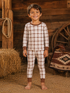 Smiling boy in brown and white plaid pajamas standing on a farm with hay and rustic decor.