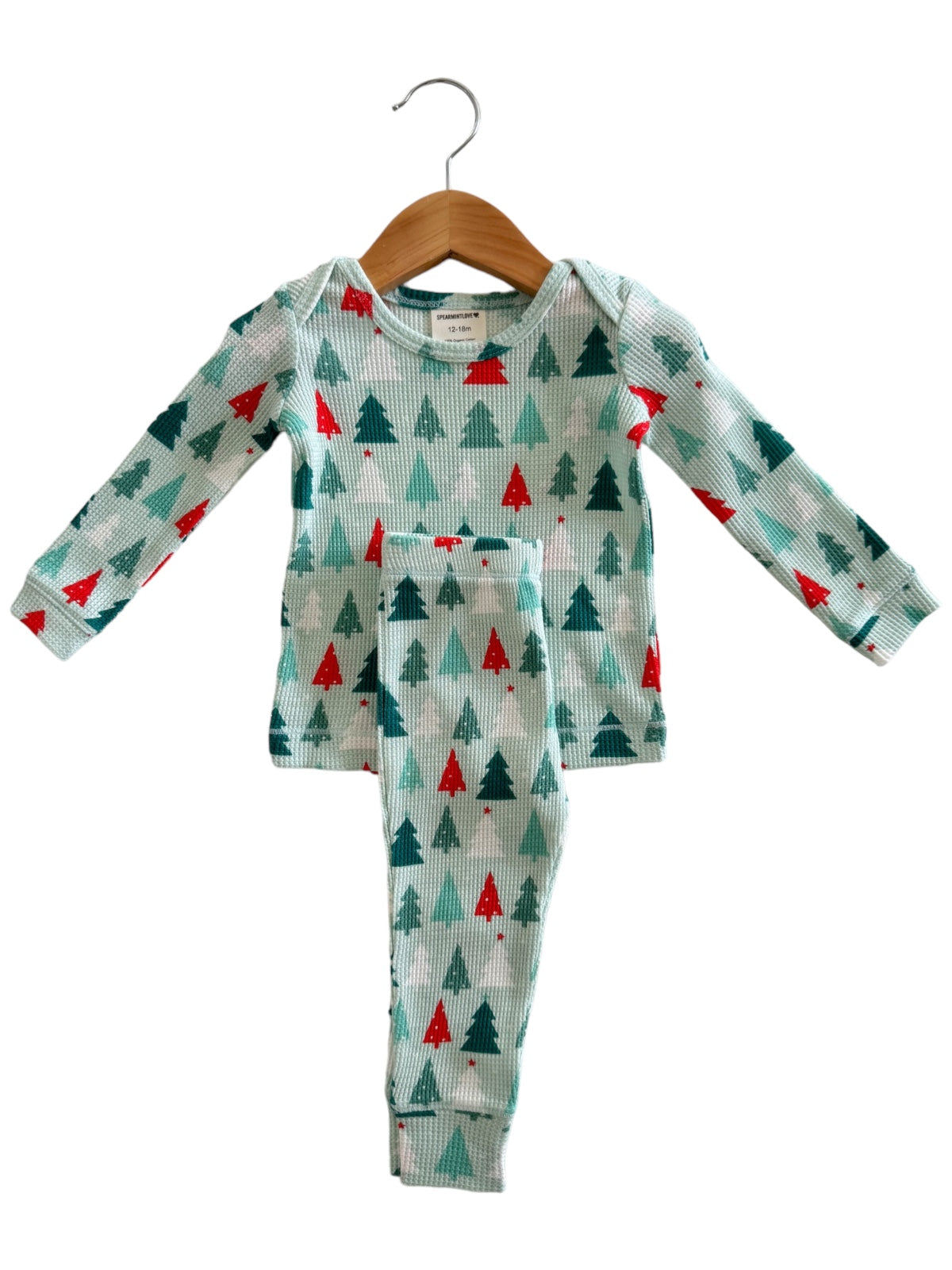 Children's pajamas featuring a holiday tree pattern in green and red, hanging on a wooden hanger.