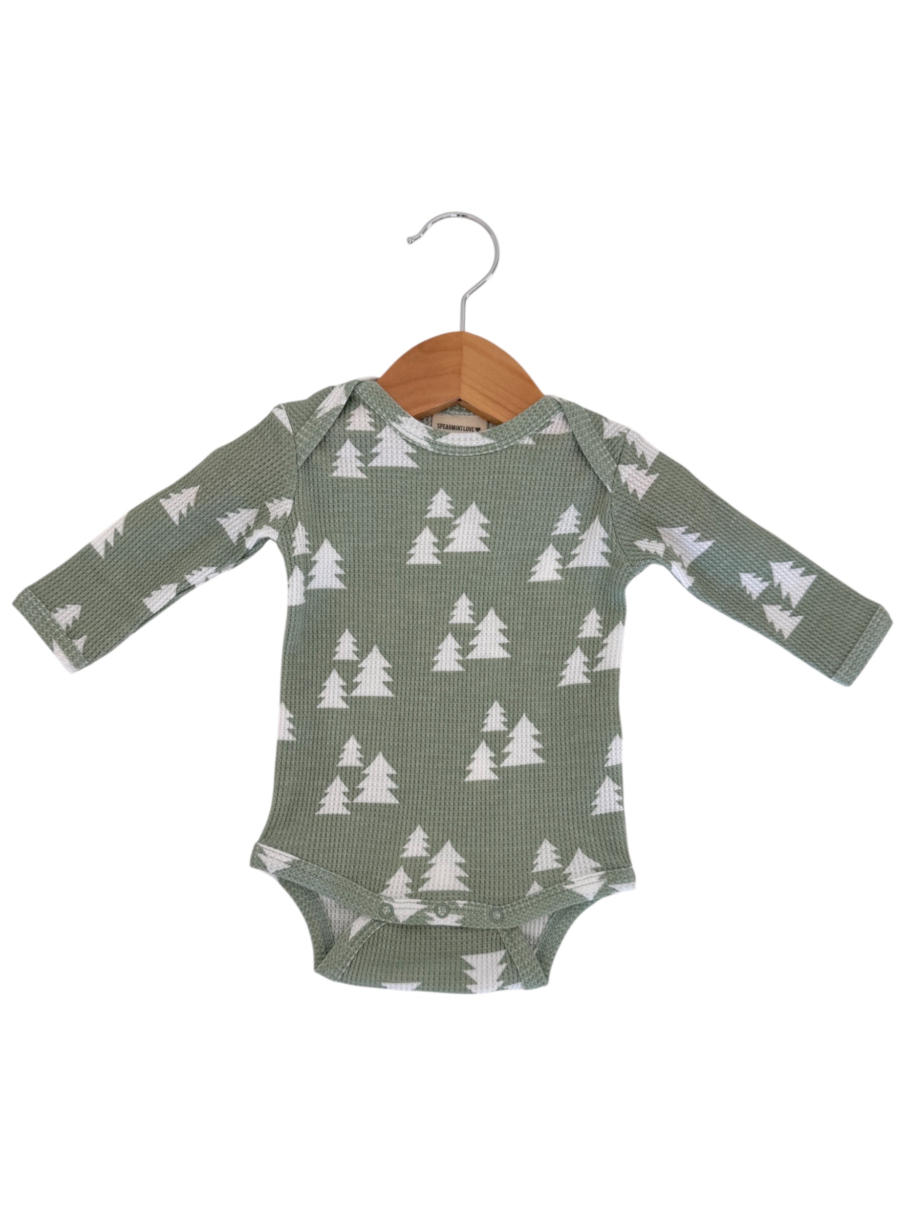 Green long-sleeve onesie with white tree pattern, hanging on a wooden hanger.