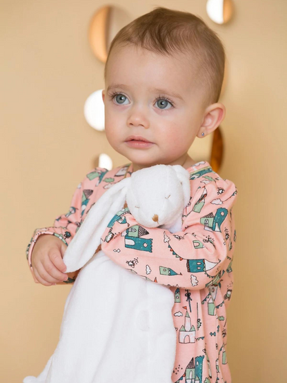 Toddler in a patterned pink outfit holding a soft white bunny toy, with a warm background.