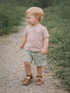 Toddler in casual wear walking on a gravel path surrounded by greenery.