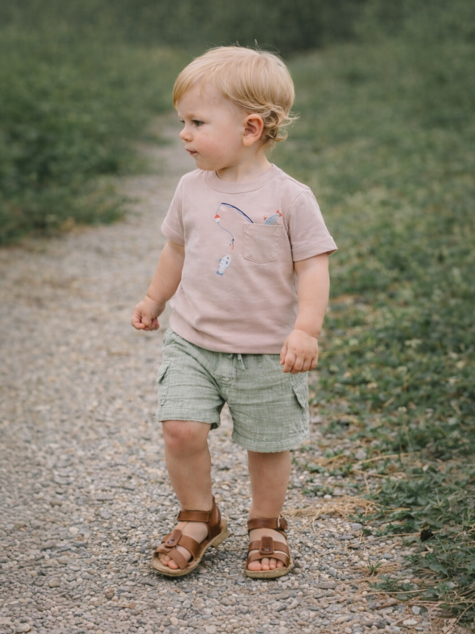 Toddler in casual wear walking on a gravel path surrounded by greenery.