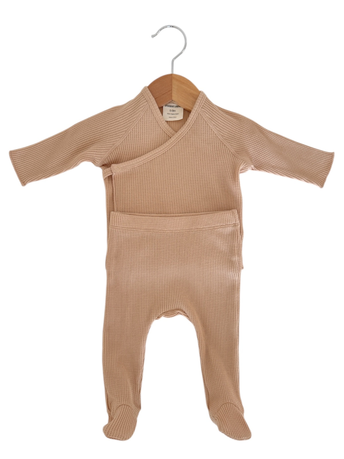 Light beige baby outfit displayed on a wooden hanger, featuring long sleeves and footed pants.