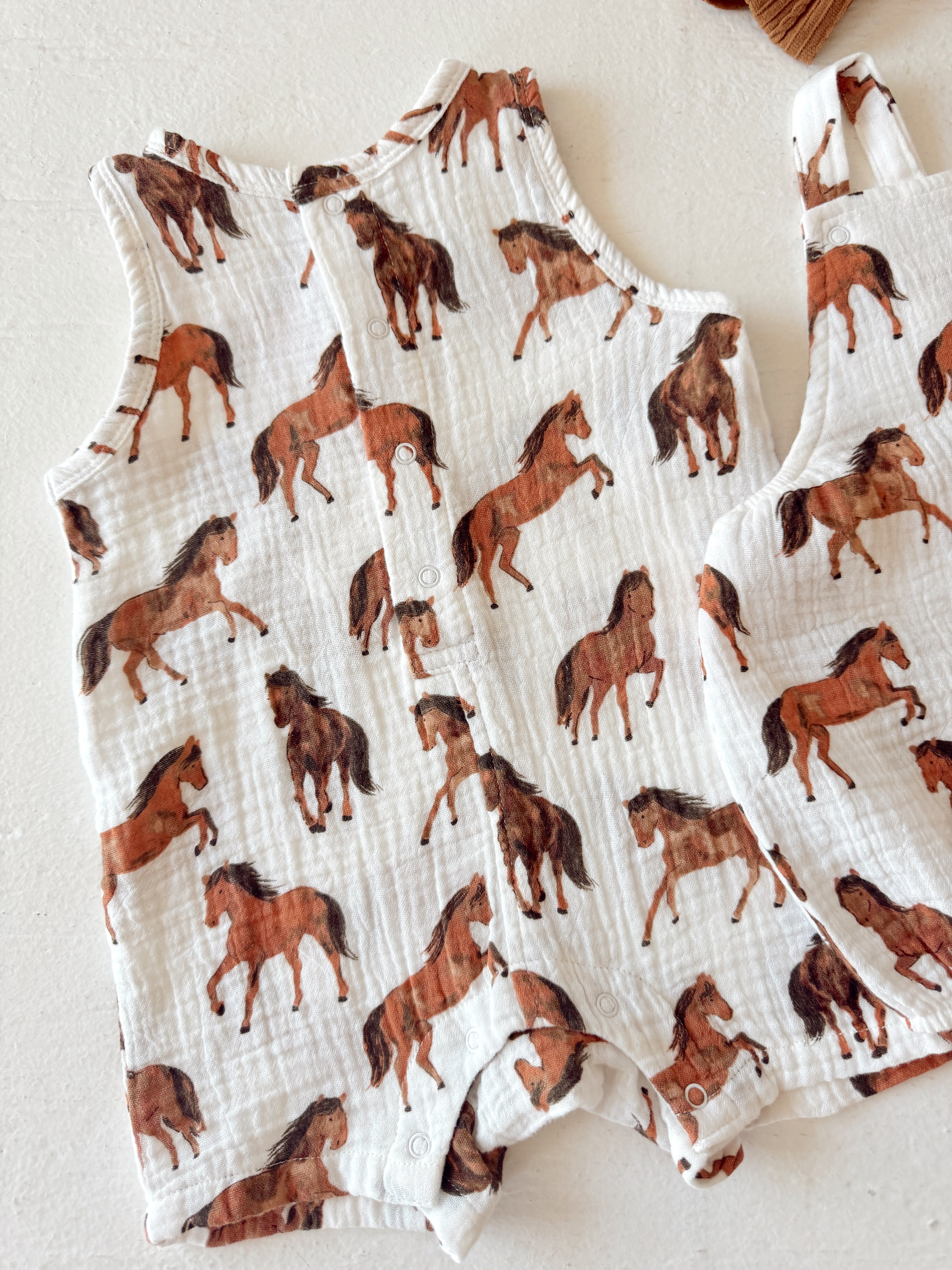 White fabric featuring a playful horse pattern, designed for children's clothing.