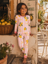 Smiling girl in lemon-patterned pajamas stands near a stone wall and lemon basket, enjoying a sunny day outdoors.