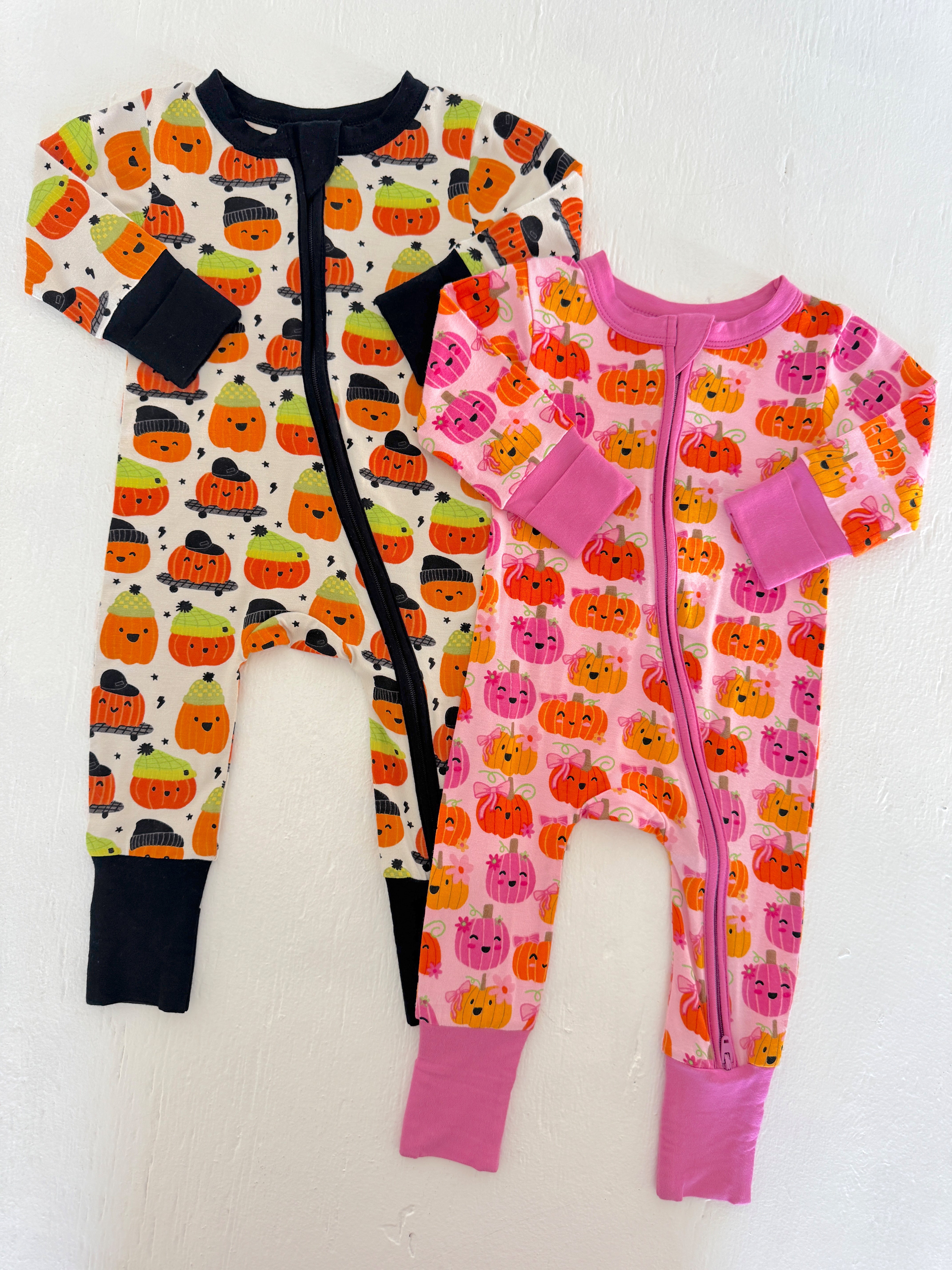 Two baby onesies with pumpkin patterns: one in black, orange, and green; the other in pink and orange.