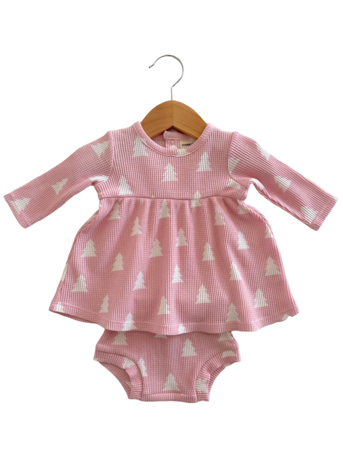 Pink dress with long sleeves and white triangle patterns, hanging on a wooden hanger, paired with a matching diaper cover.