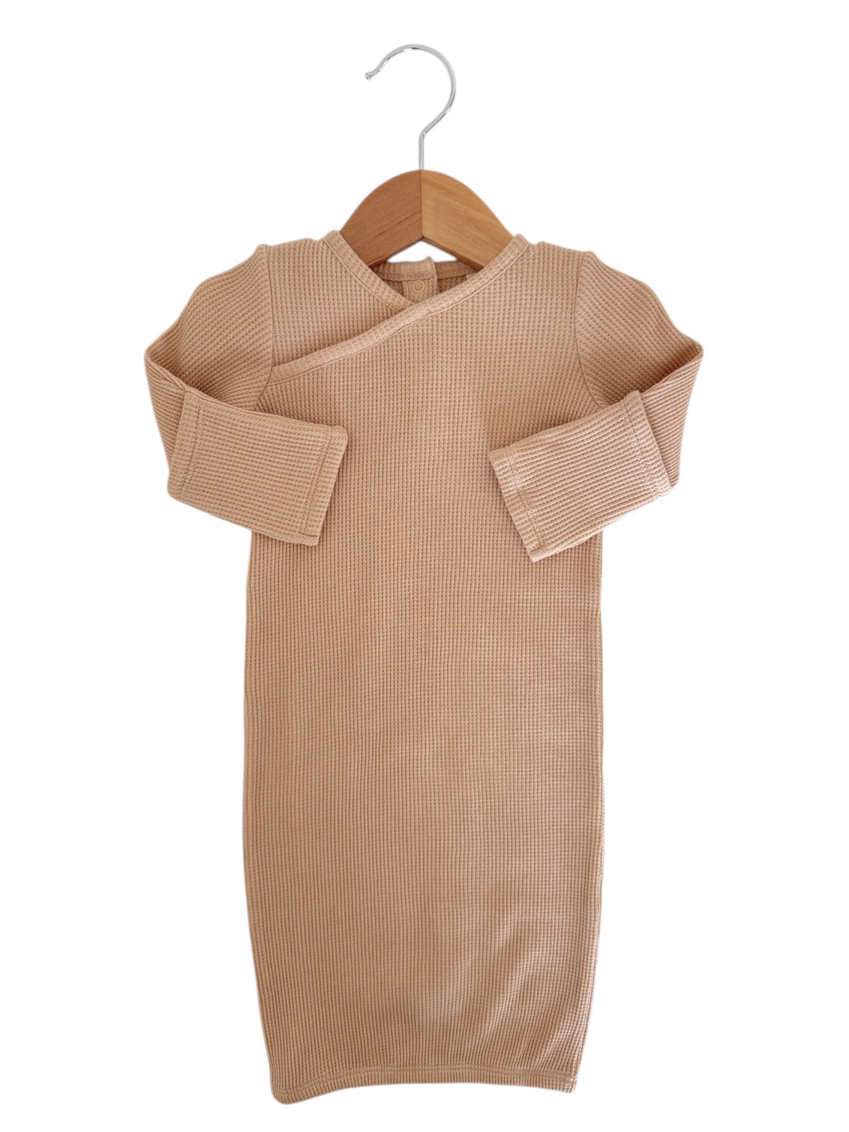 Beige, long-sleeve, ribbed baby dress hanging on a wooden hanger against a white background.