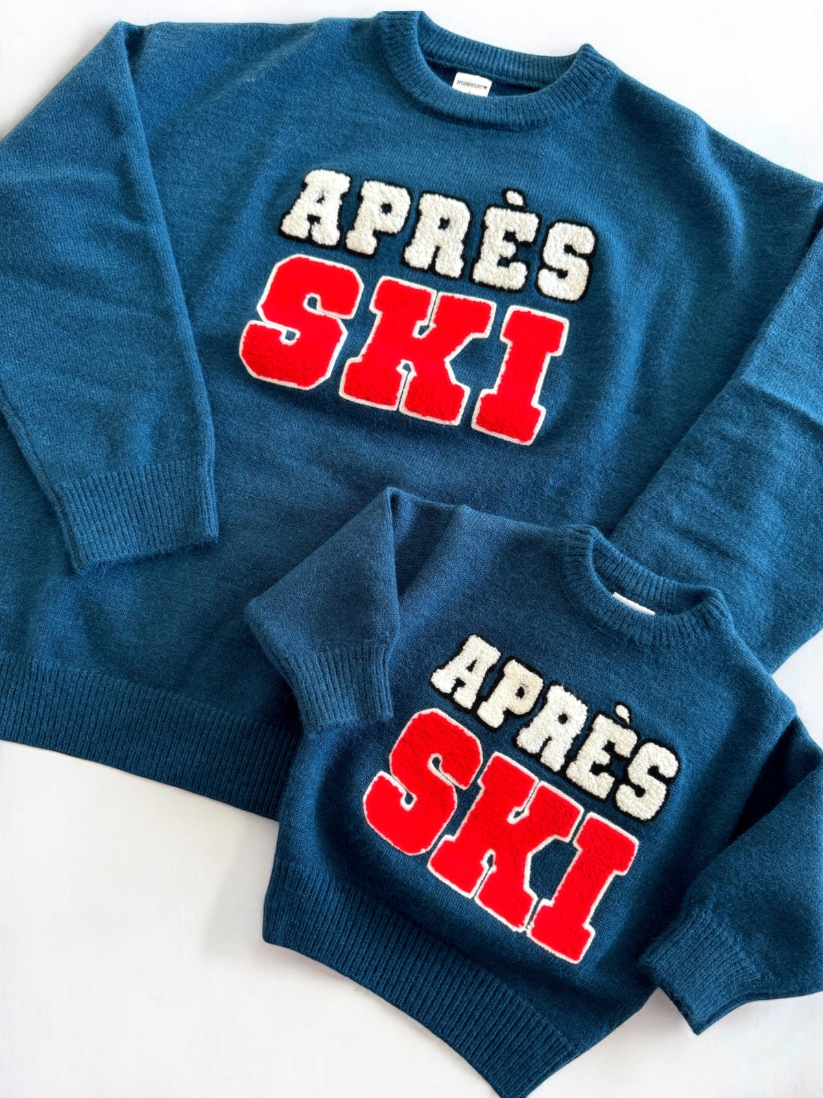 Matching blue "APRÈS SKI" sweaters for adults and kids, featuring textured white and red letters.
