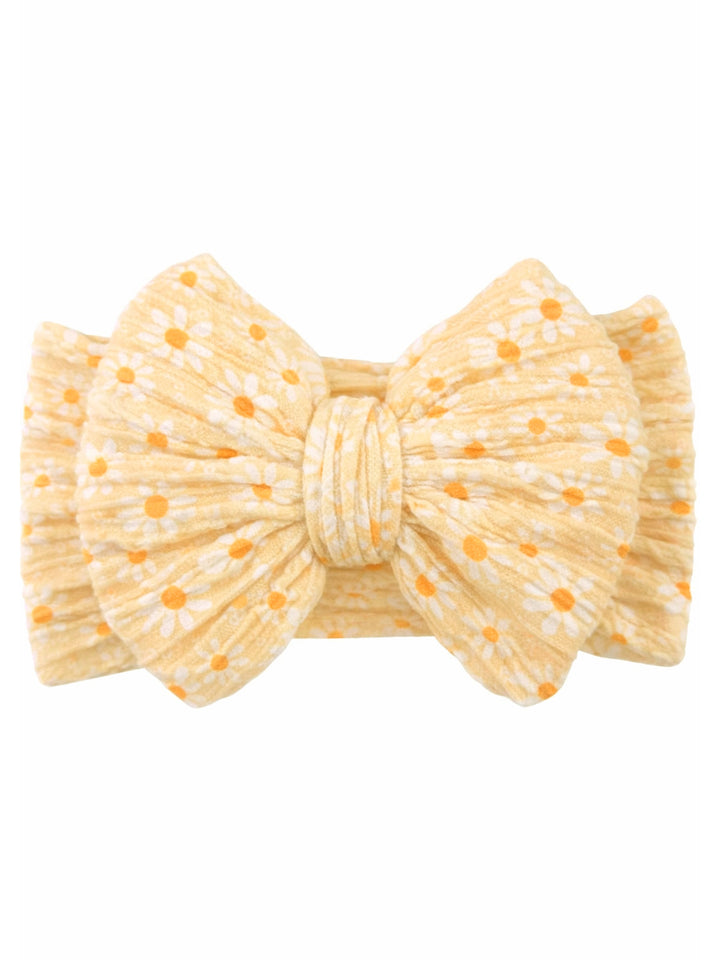 Yellow bow headband with white flowers and orange dots against a plain background. Ideal for stylish accessories.