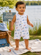 Smiling toddler in a fishing-themed outfit stands on a blanket by a lake, with a "Gone Fishing" sign nearby.