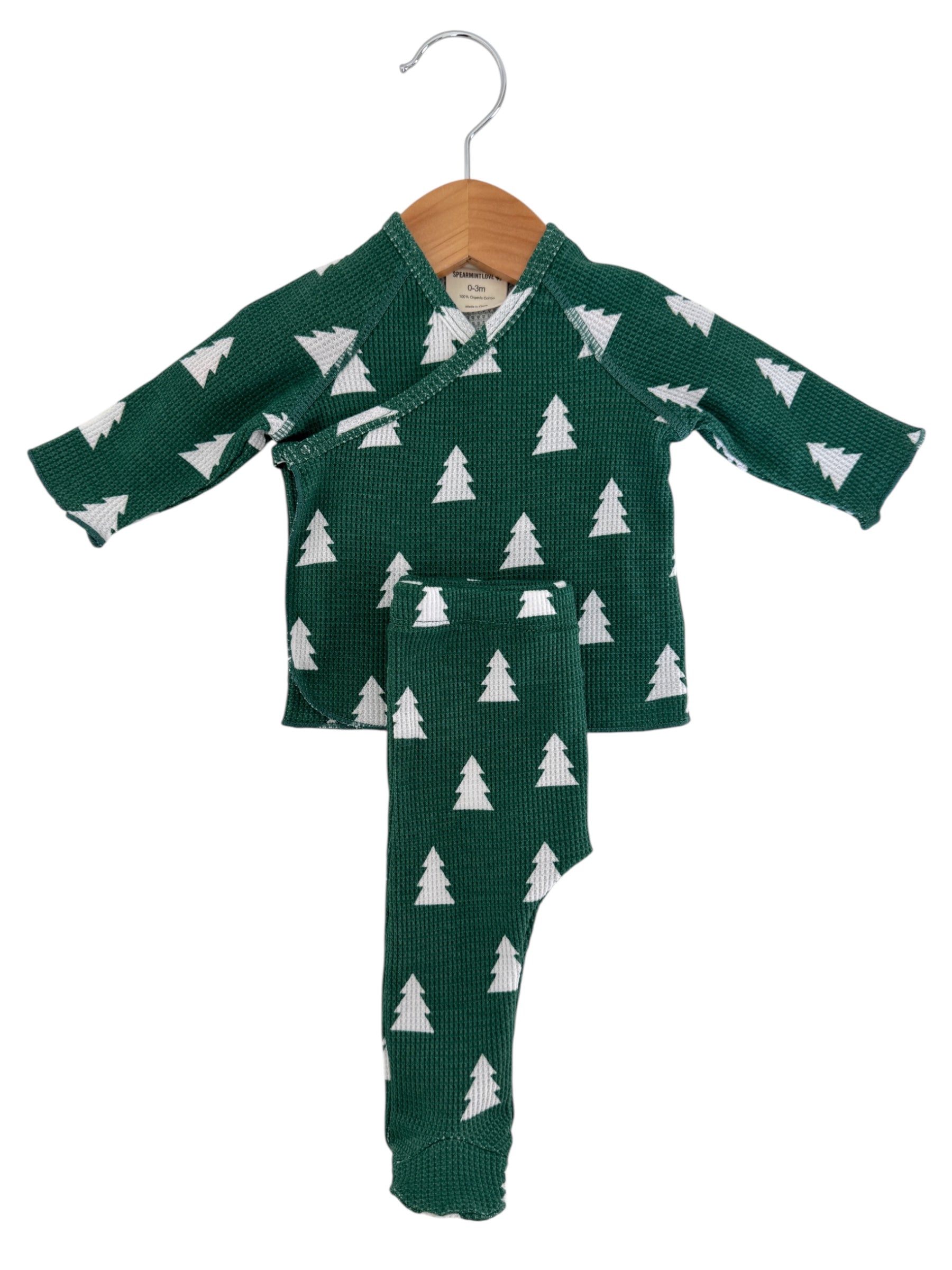 Green baby outfit with white tree patterns, consisting of a top and matching pants, hanging on a wooden hanger.