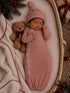Newborn baby in a striped outfit sleeping beside a teddy bear in a cozy basket with festive decorations.