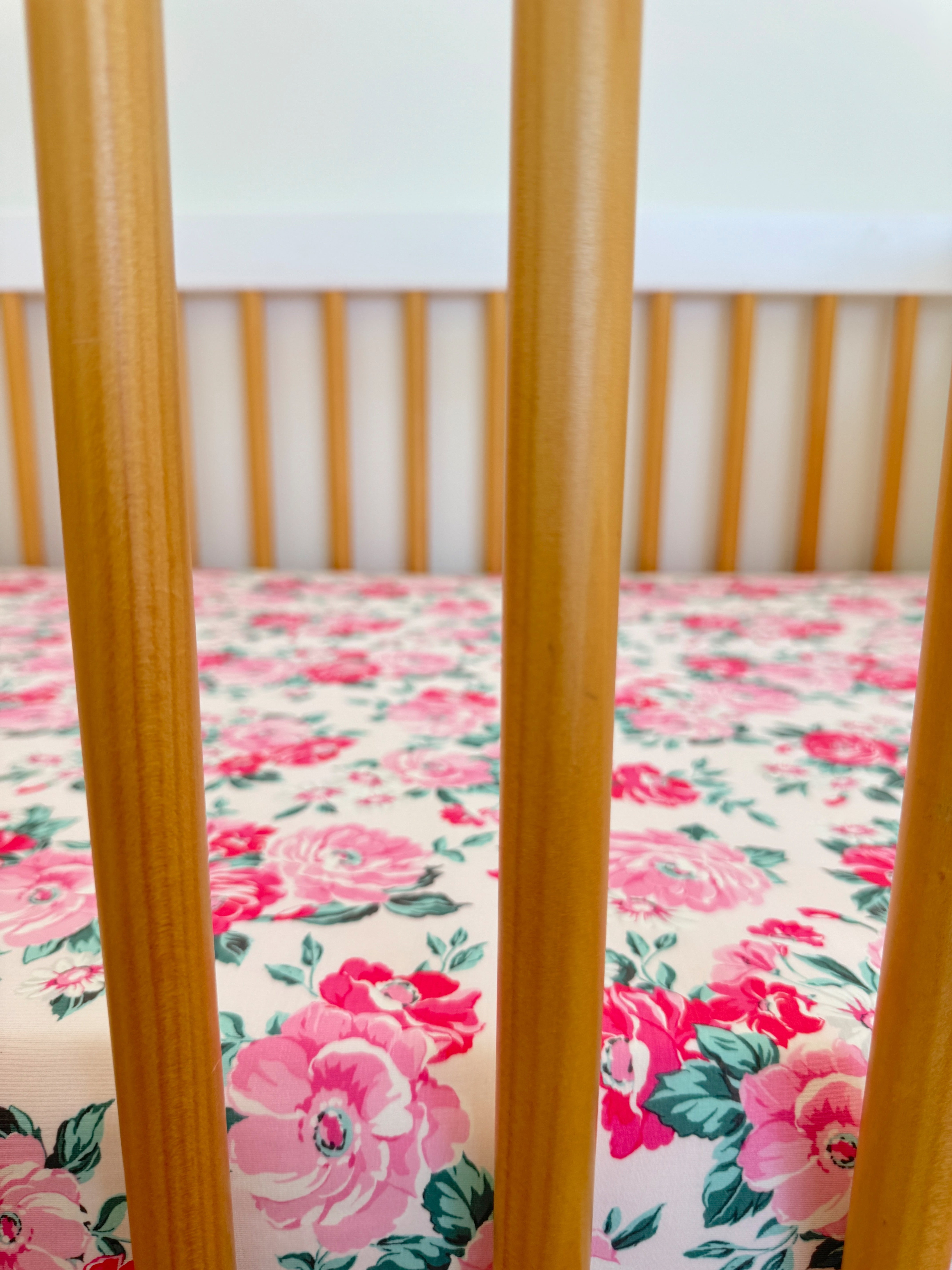 Wooden crib bars frame a floral-patterned sheet featuring pink roses and green leaves.