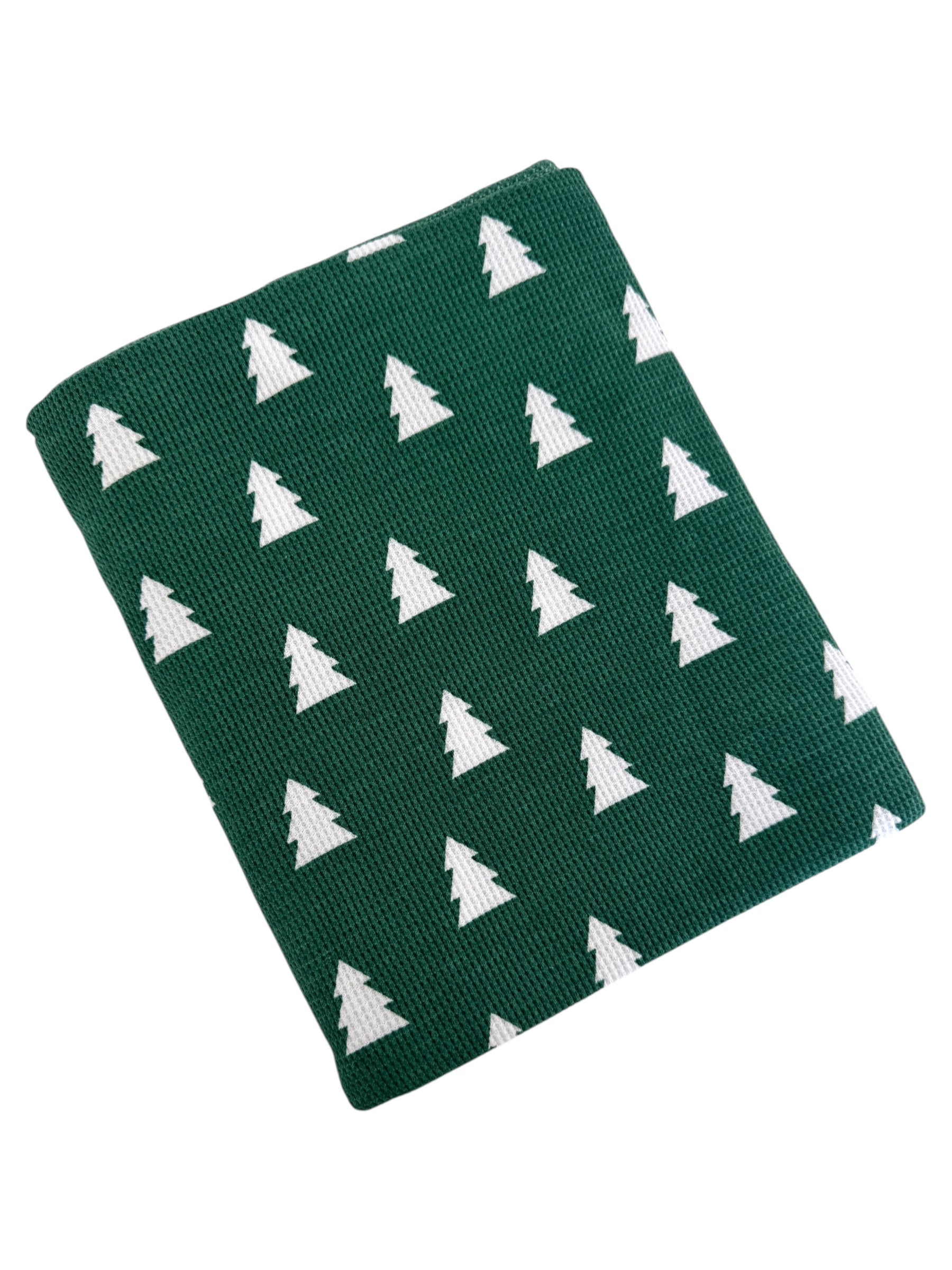 Green blanket with white tree pattern, folded neatly for cozy holiday decoration.