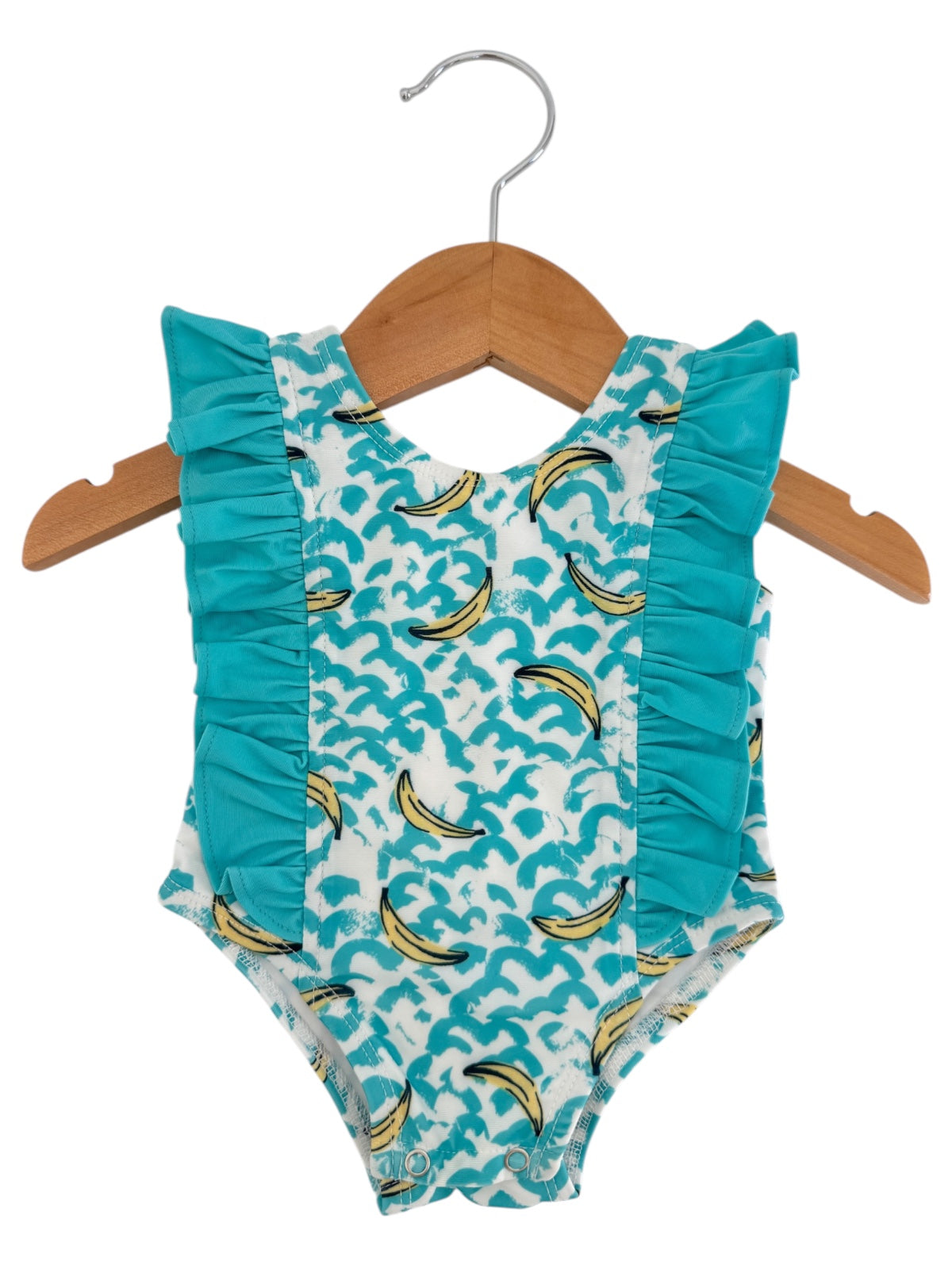 Turquoise baby swimsuit with ruffles and banana print, hanging on a wooden hanger.