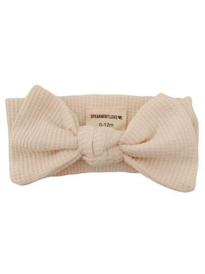Beige baby headband with a large bow designed for ages 0-12 months, featuring a textured fabric.