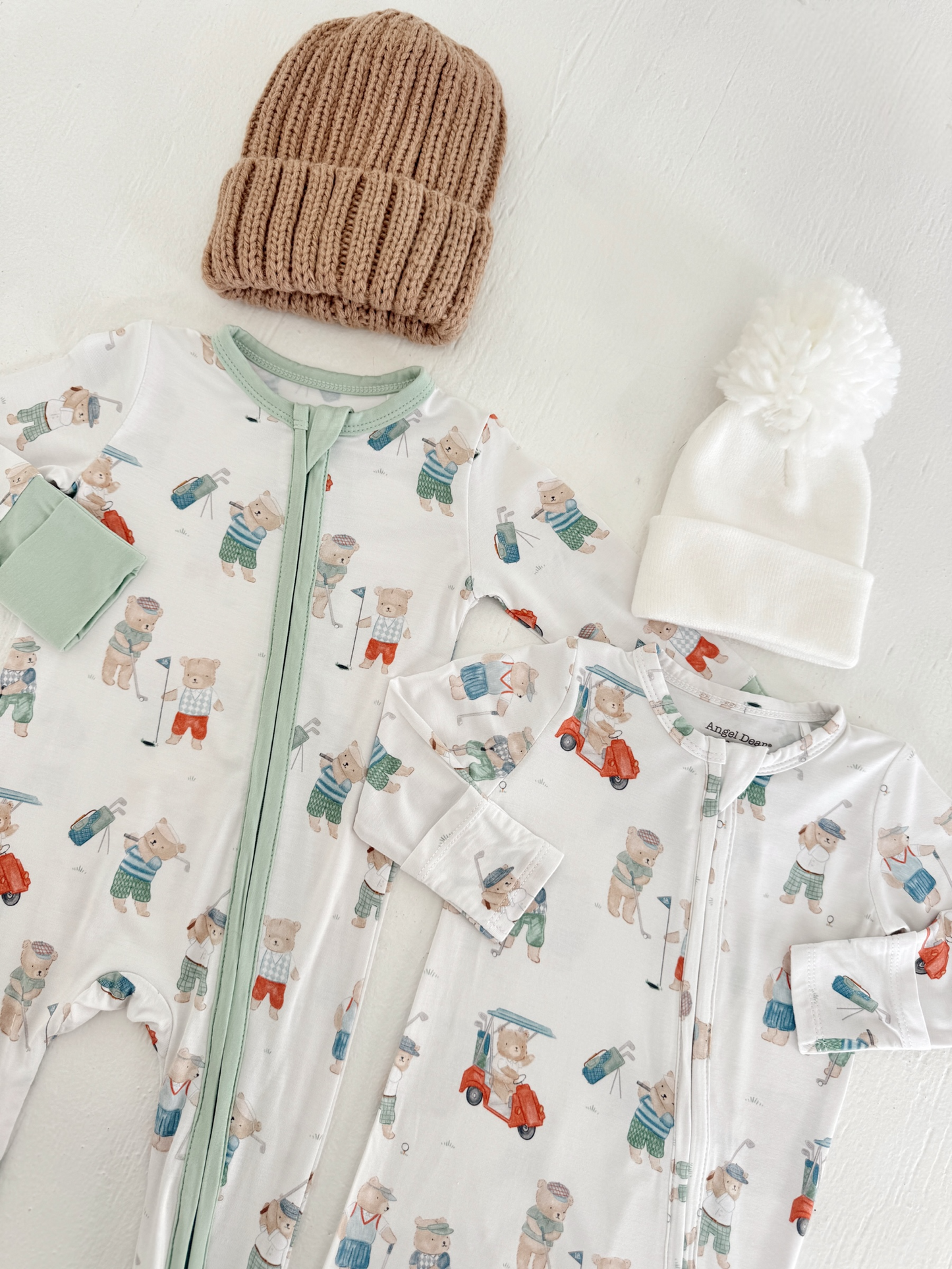 Two infant onesies with bear designs and two knitted hats on a white background.