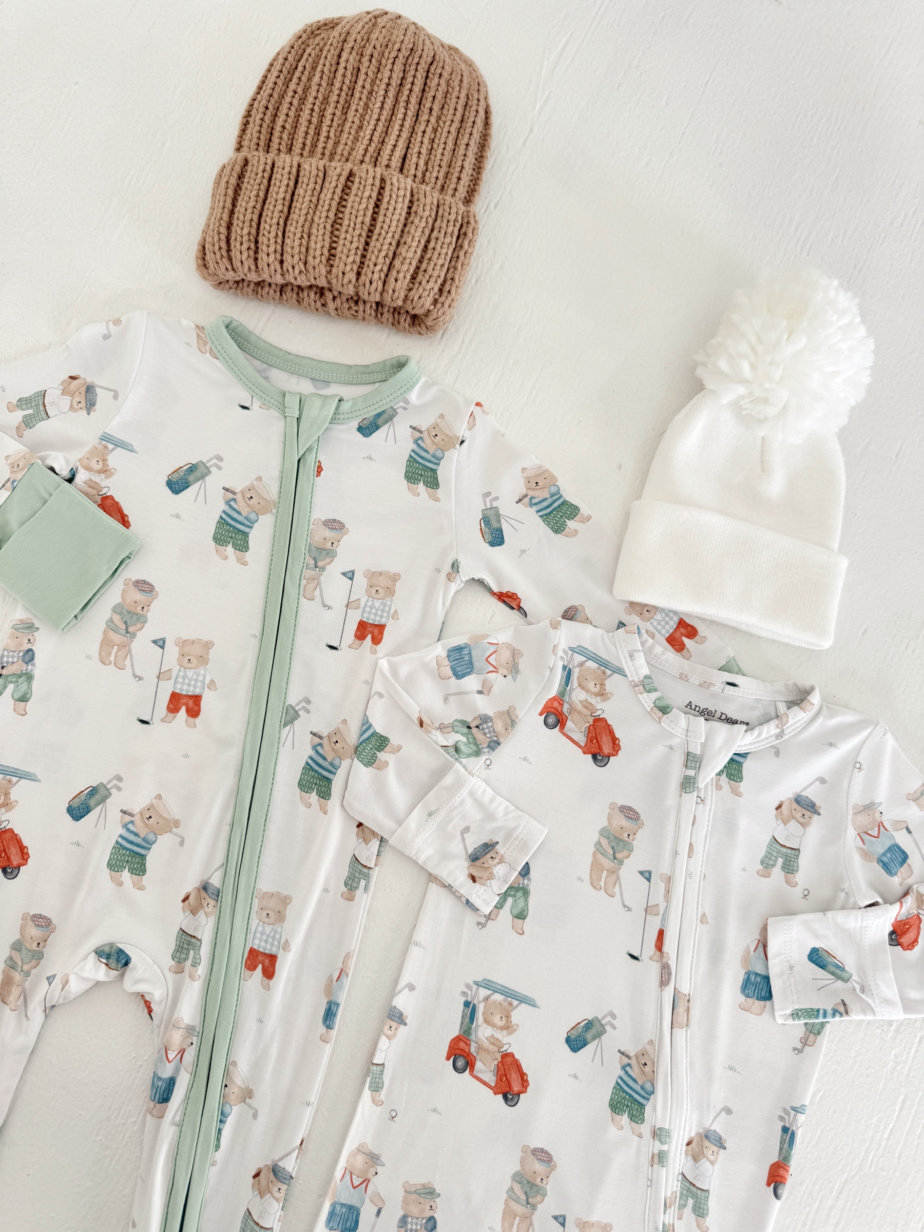 Two infant onesies with bear designs and two knitted hats on a white background.
