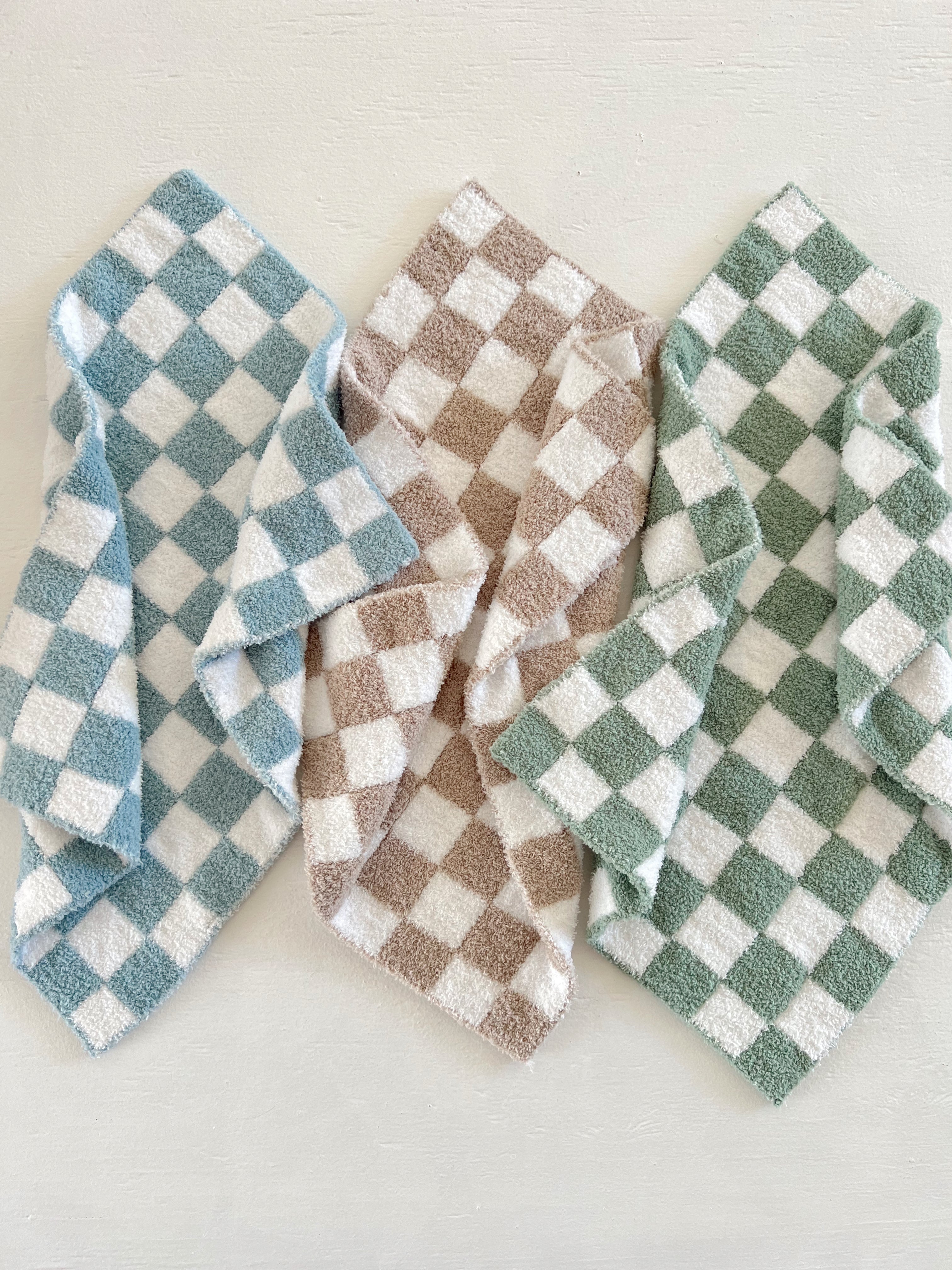 Three checkered towels in blue, brown, and green arranged aesthetically on a light textured background.