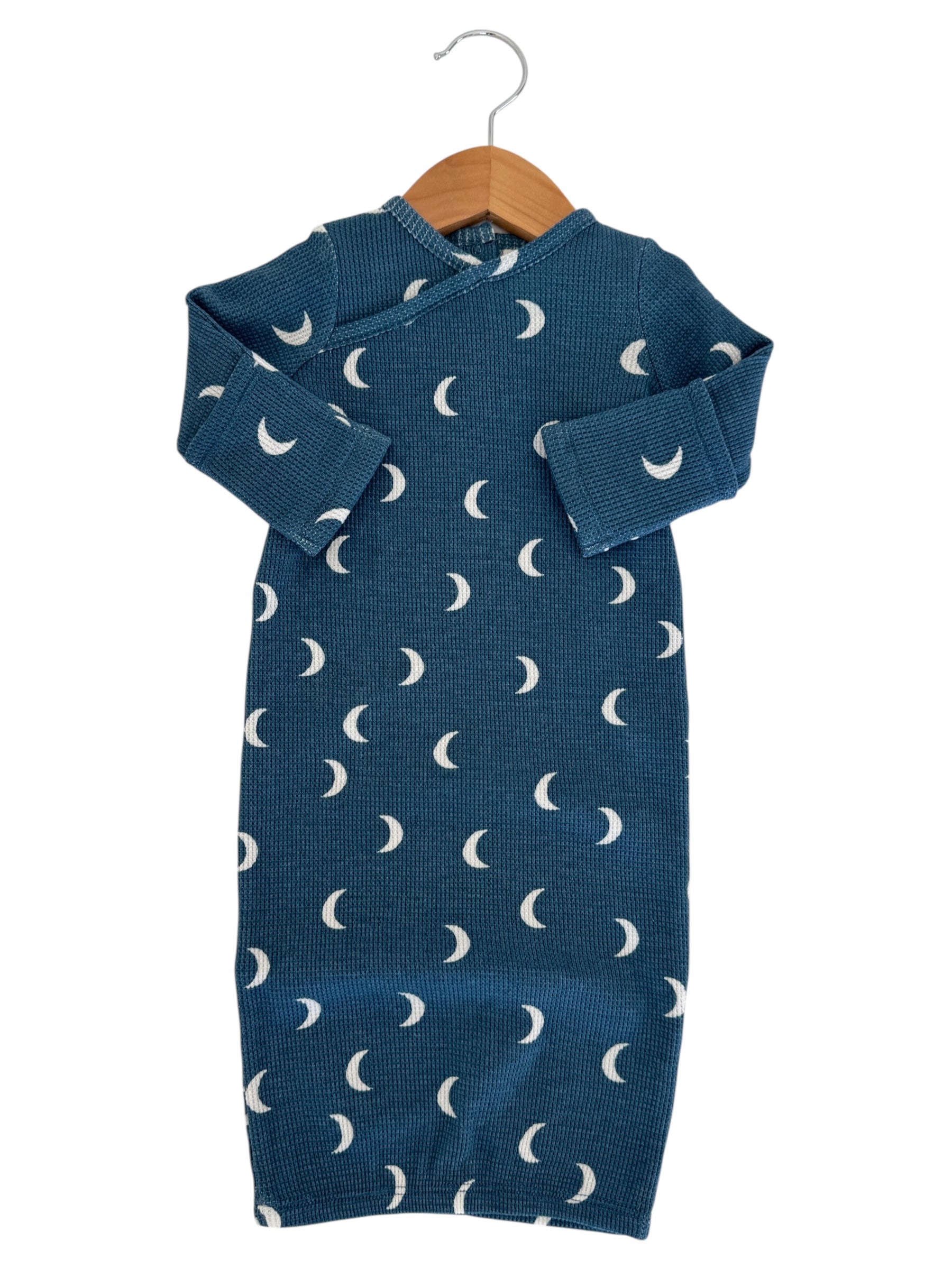 Teal baby dress with white moon patterns, hanging on a wooden hanger against a white background.