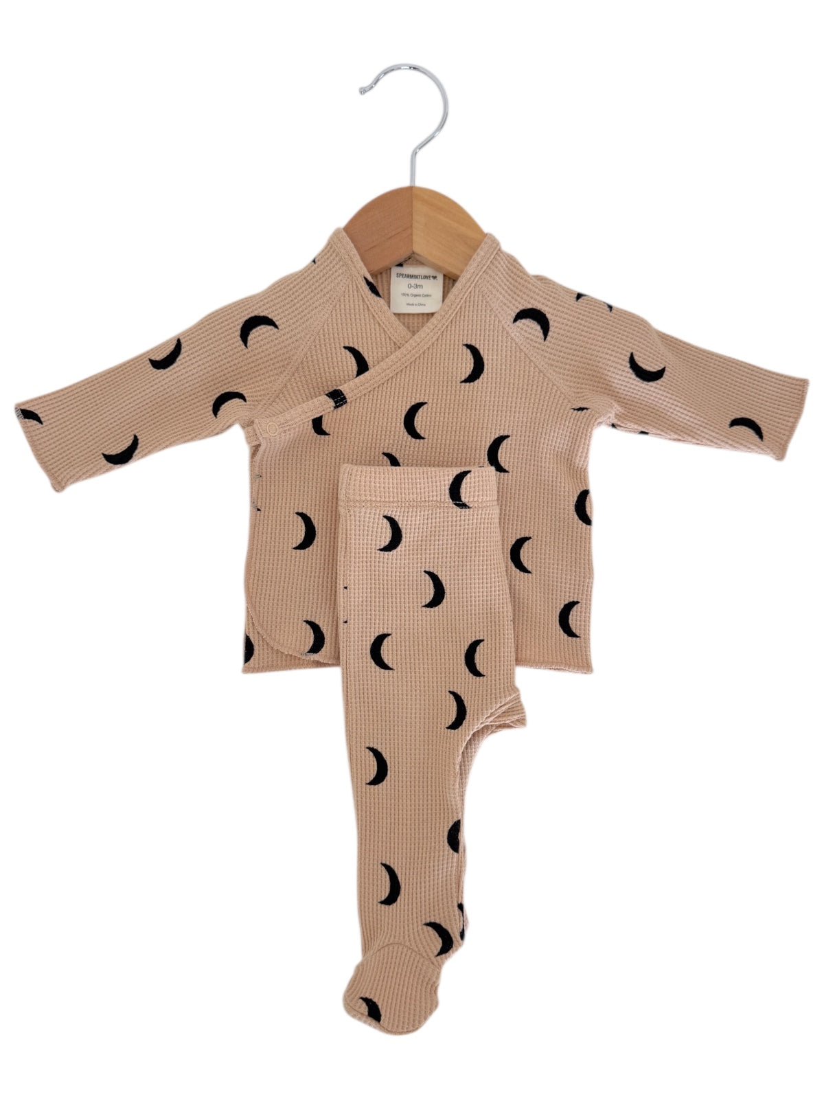 Beige infant outfit featuring long sleeves and black crescent moon patterns, hanging on a wooden hanger.