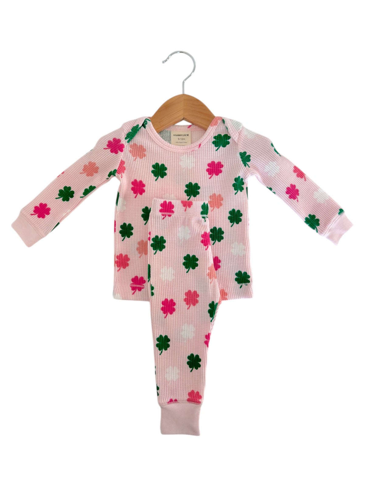 Pink matching pajamas with clover patterns, hanging on a wooden hanger against a white background.