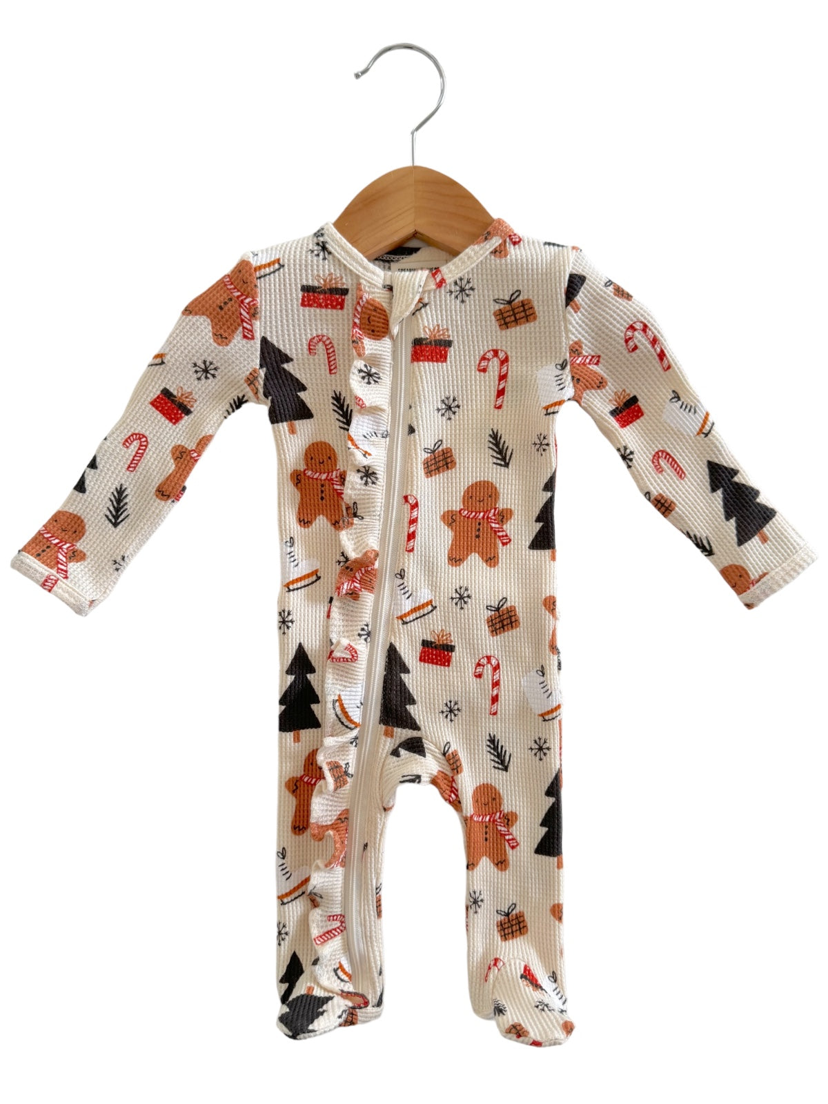 Festive infant onesie with gingerbread men, candy canes, and Christmas trees on a cream background, hanging on a hook.