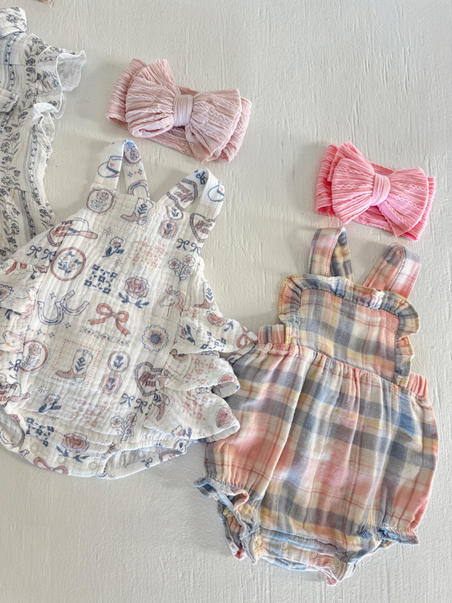 Two toddler outfits and hair bows on a white background, featuring floral and checked patterns in soft colors.