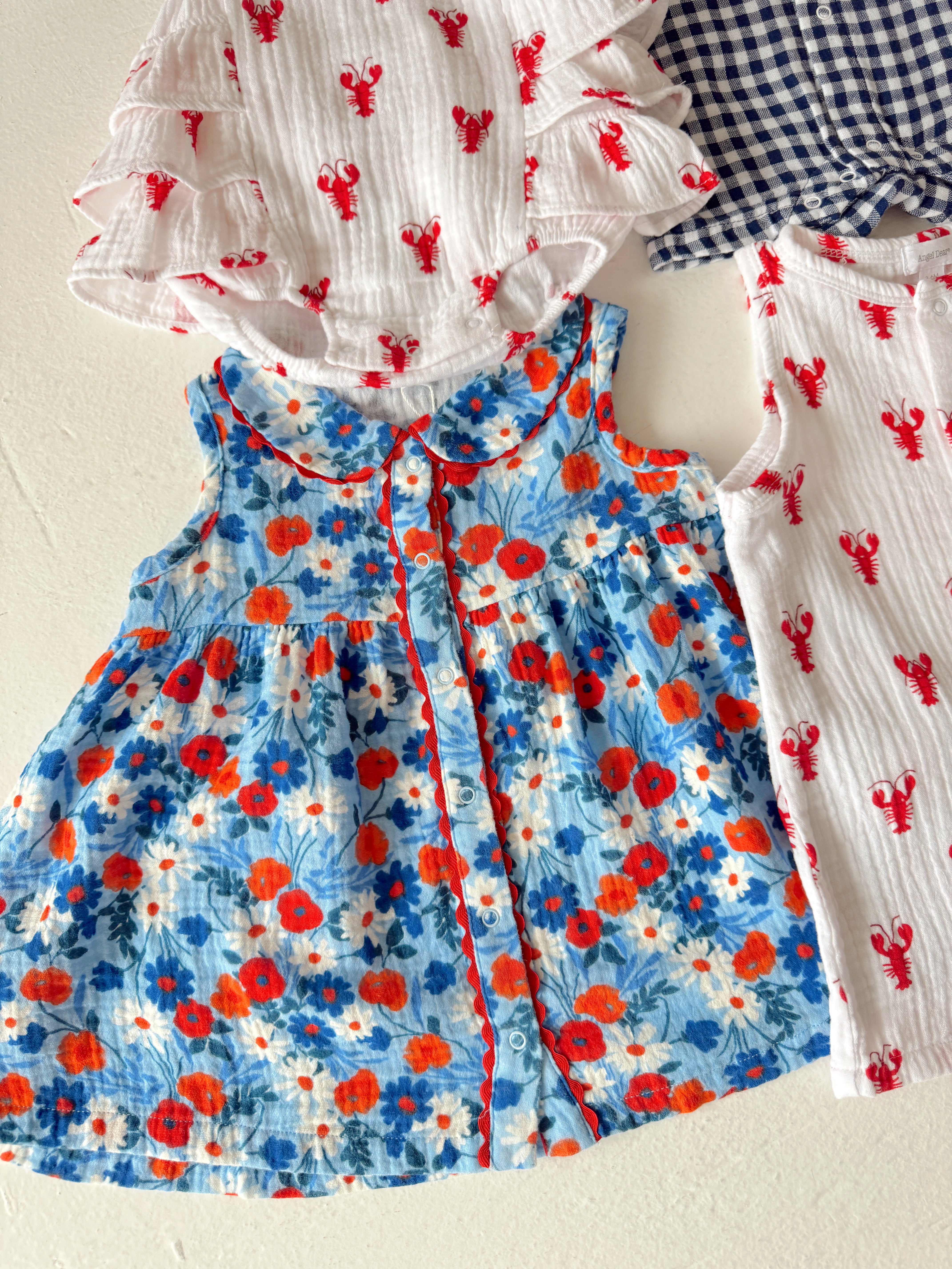 Colorful children's clothing, including a floral dress and lobster print items, arranged on a light background.