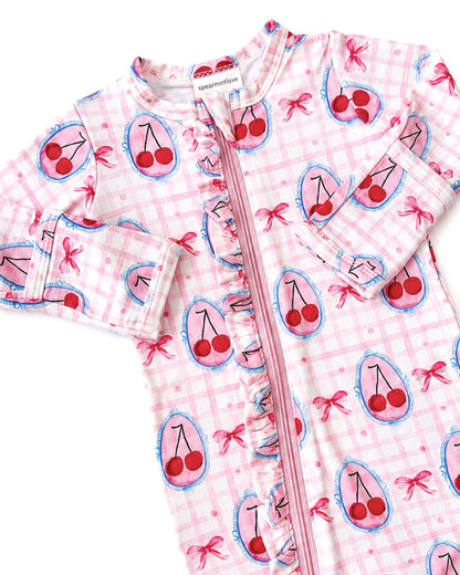 Pink onesie with cherry and bow prints, featuring a front zipper and ruffled details.