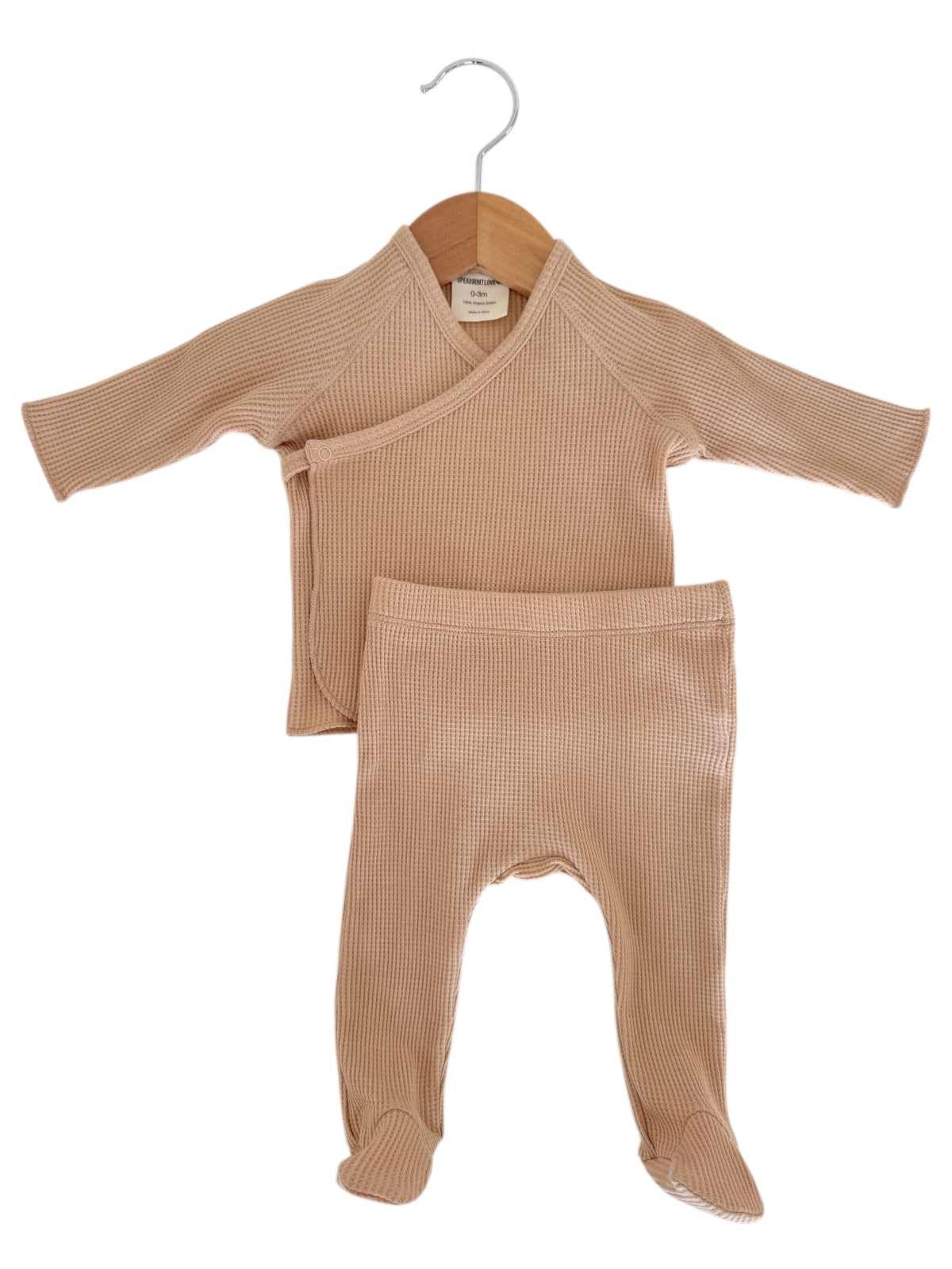 Light brown infant two-piece outfit with a wrap top and footed pants, displayed on a wooden hanger.