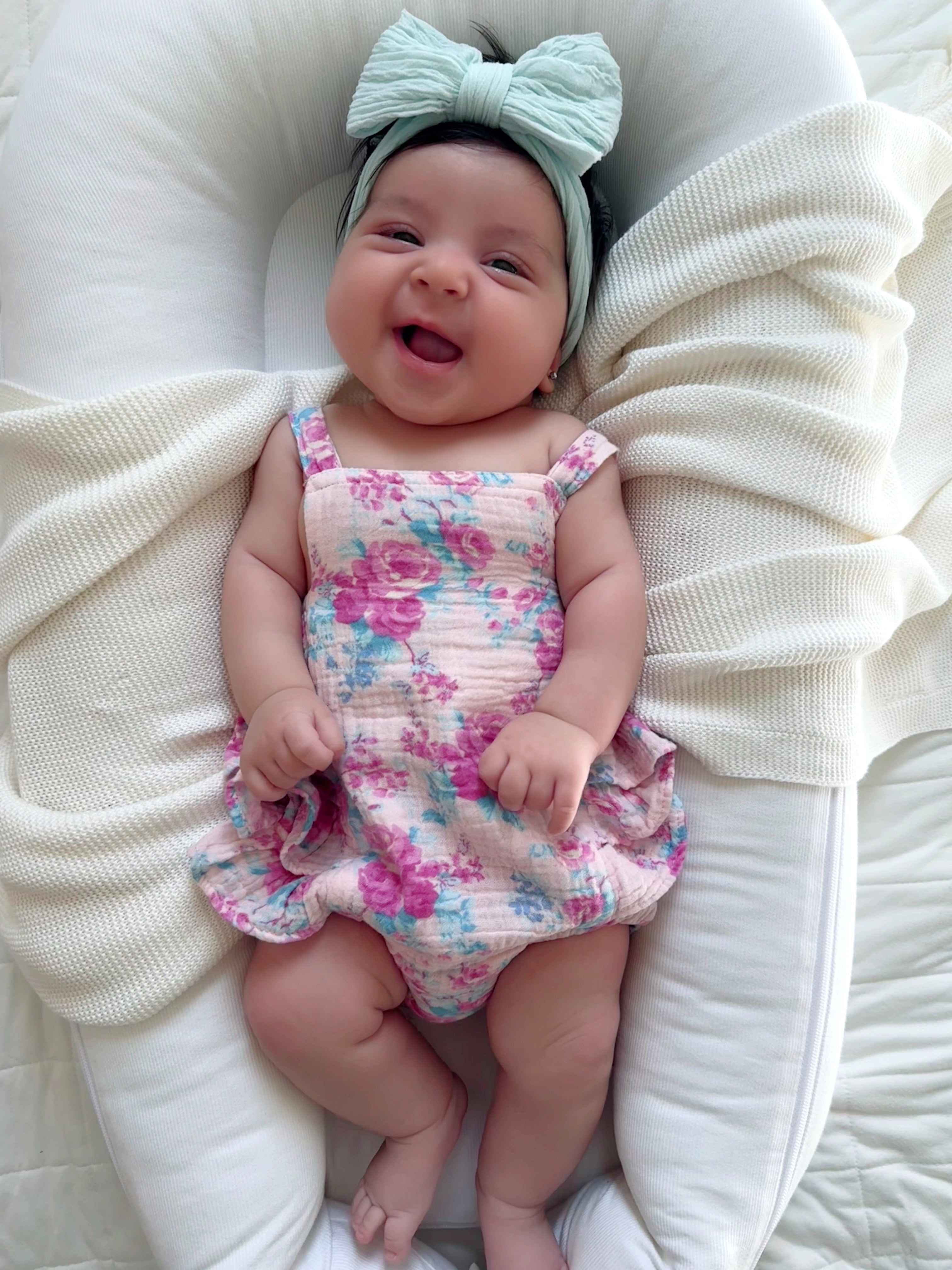 Smiling baby in floral outfit with a mint bow, resting on a cozy blanket.