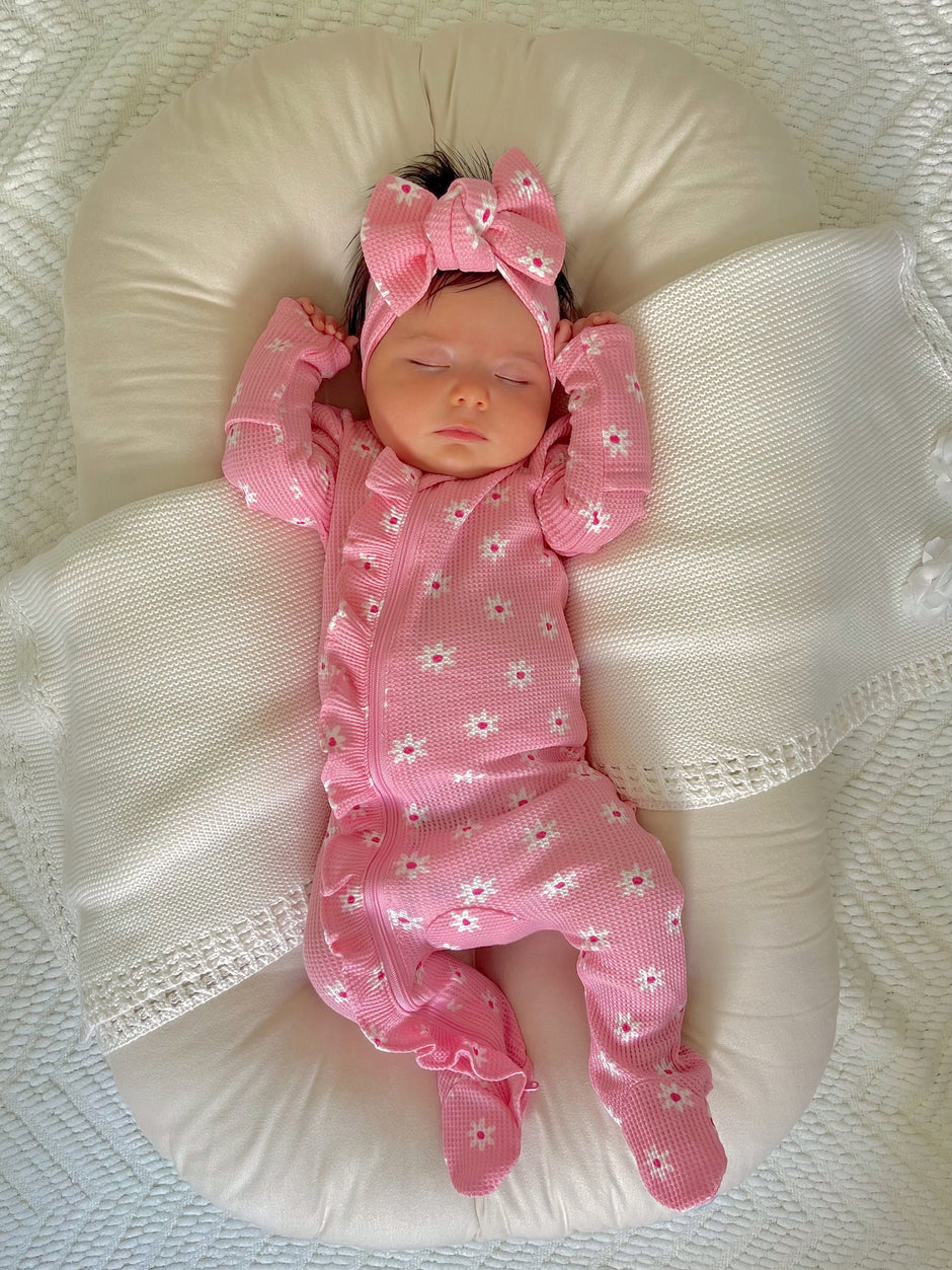 Baby girl in pink floral pajamas and bow, peacefully sleeping on a soft, white pillow.
