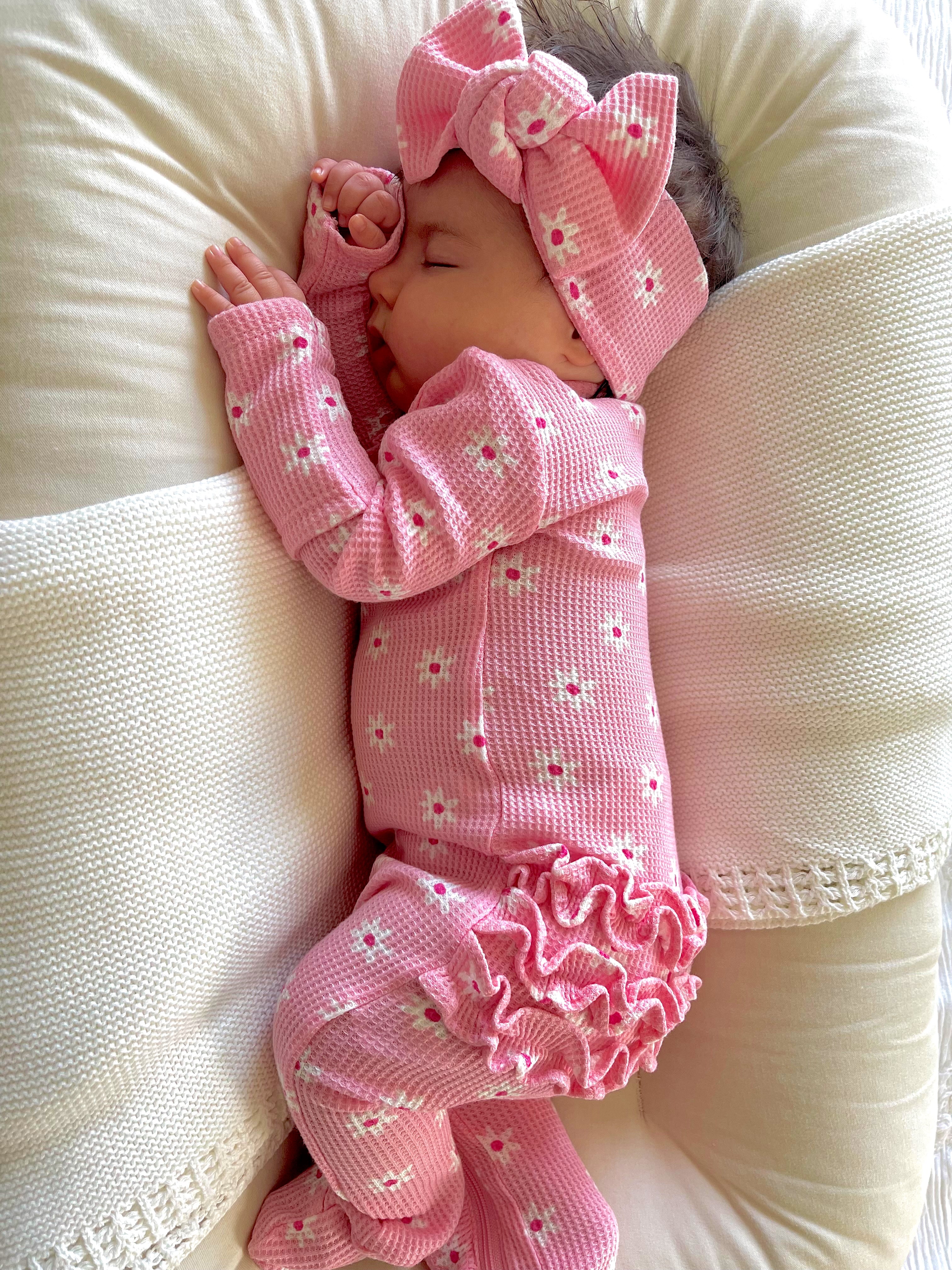 Sleeping baby in pink floral pajamas, wearing a matching headband, nestled between soft pillows.