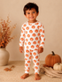 Smiling child in pumpkin-patterned pajamas, standing next to pumpkins and fall decor. Cozy autumn setting.