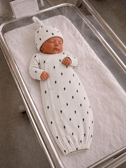 Newborn asleep in a cozy white outfit with lightning bolt patterns, resting in a hospital bassinet.
