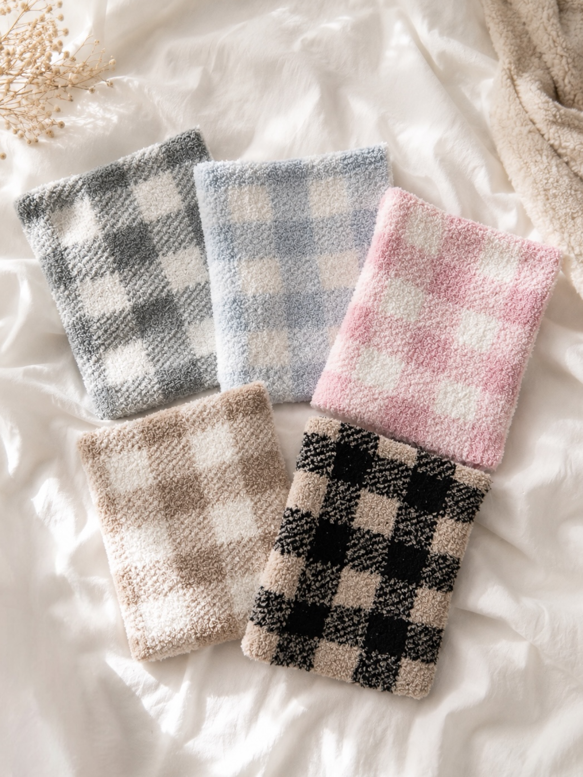 Five cozy, checked towels in gray, blue, pink, beige, and black arranged on a soft white surface.