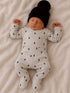 Newborn baby peacefully sleeping in gray outfit with lightning patterns and black hat on a soft blanket.
