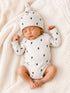 Sleeping baby in a white onesie with lightning bolt prints, wearing a matching hat, on a soft, textured blanket.