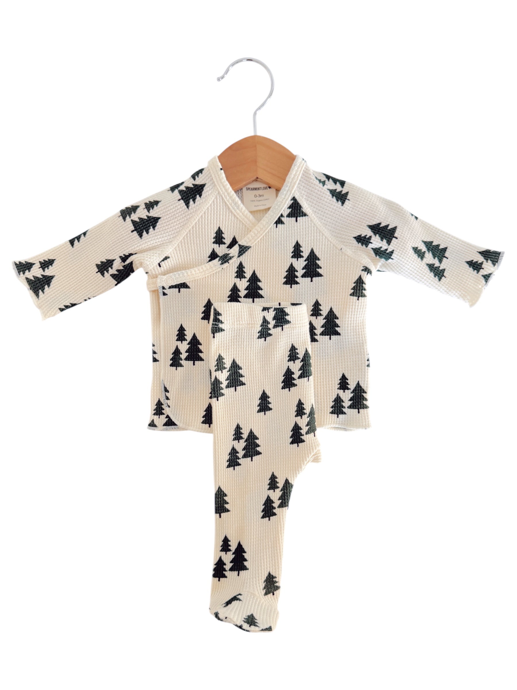 Cream-colored children's pajama set with a tree pattern, displayed on a wooden hanger.