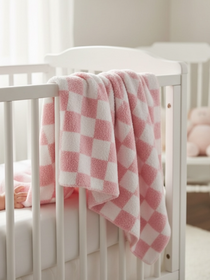 Pink and white checkered blanket draped over a crib with a child's feet visible. Soft, cozy nursery setting.