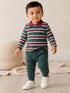 Toddler wearing a striped long-sleeve polo and green joggers, walking on wood floor with a neutral background.